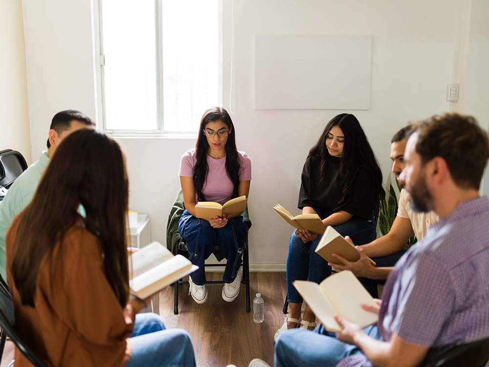 Group of six adults sitting in a circle with open books in their hands