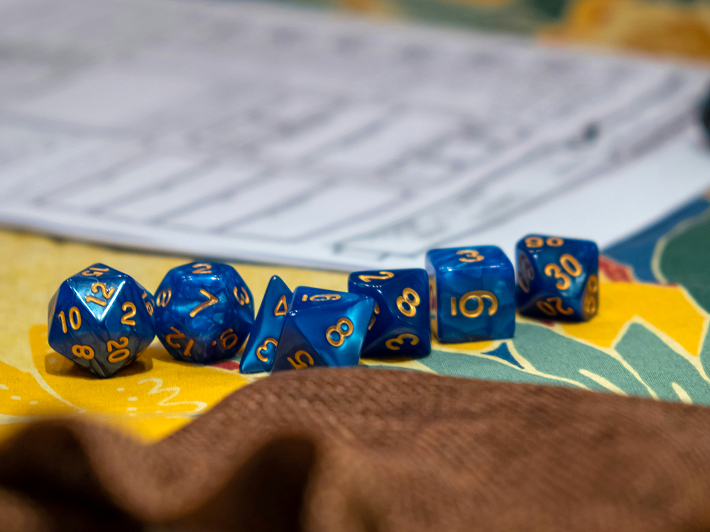 set of blue dice on desk next to a Dungeons and Dragons character sheet