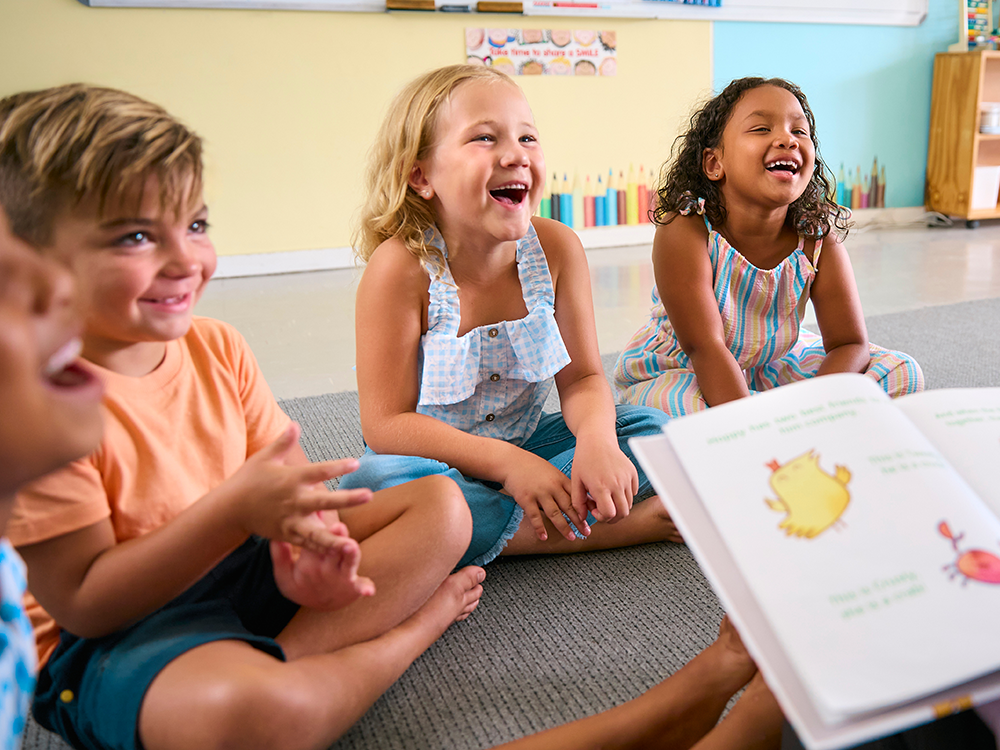 Group of four children, two boys and two girls, smiling as someone reads to them