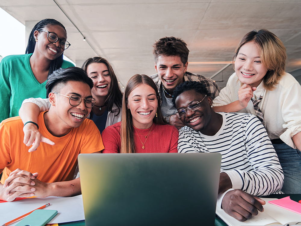 Group of seven teens huddled around a laptop and smiling