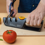 person sharpening scissors with knife sharpener, tomato in foreground