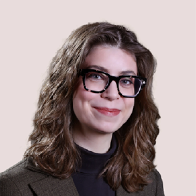Woman with brown hair, glasses, black turtleneck shirt, and a brown coat